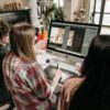 A group of young adults working on a design project using a desktop computer in an artistic workspace.